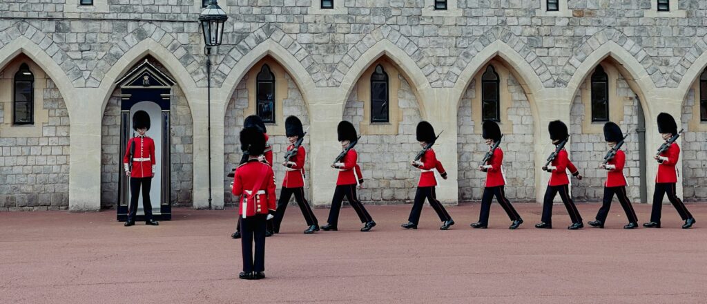 Changing the Guard ceremony at Windsor Castle, with soldiers in red tunics and bearskin hats marching past the castle's stone walls